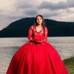 Young woman in red quinceañera dress by a picturesque lake, capturing a special moment.